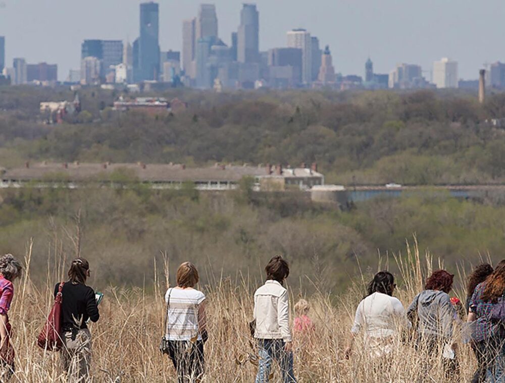 Particpants on Learning from Place: Bdote are photographed near Pilot Knob with the Minneapolis skyline in the background.