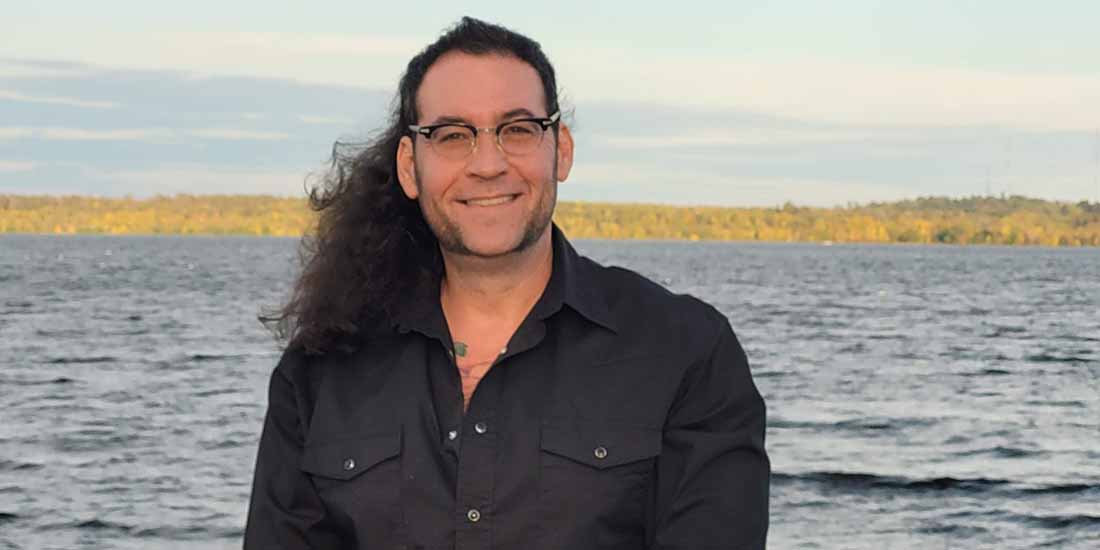 Photo of Dr. Dennis Fisher in front of a lake with a tree-lined shore in the background.