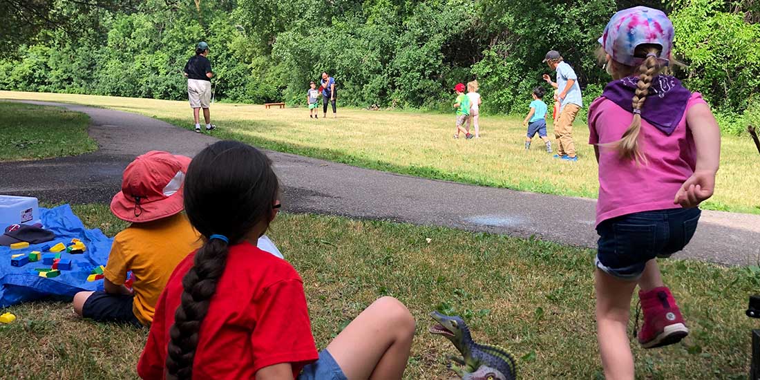 Children play in a park as other children watch on and one runs to join the fun.