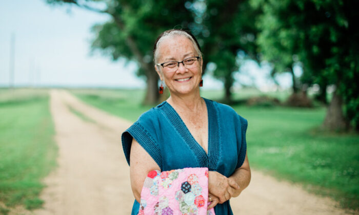 Minnesota's Poet Laureate, Gwen Nell Westerman poses for a photo along a gravel road with trees and fields in the background.