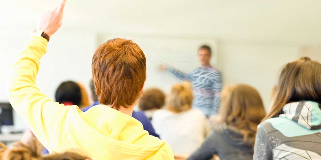 Male high school student raising hand to ask question in class.