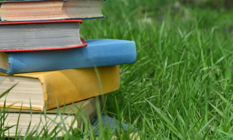 Colorful hardcover books stacked atop one another on a field of grass.