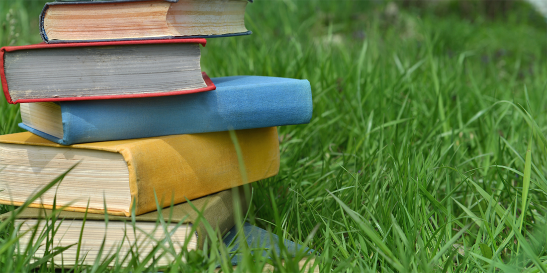 Colorful hardcover books stacked atop one another on a field of grass.