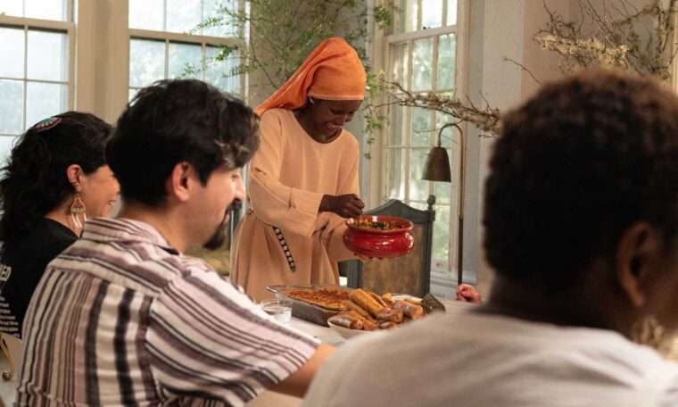 A woman in a colorful headscarf serves food from a bowl.