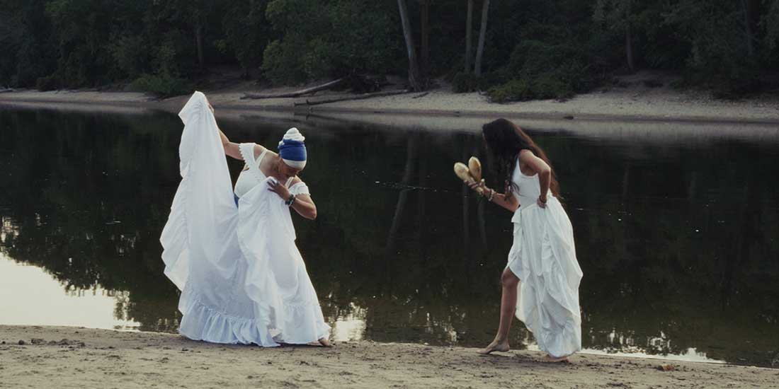 Still from the film NUESTRO NORTE shows two women dressed in white dancing by a river.