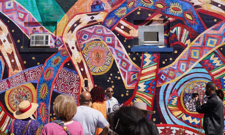 Participants on a Learning from Place: St. Paul's Little Africa trip pause in front of a mural.
